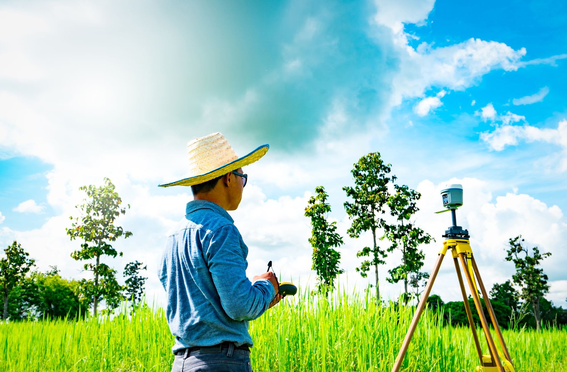 Asian smart engineer or surveyor working on controller screen for surveying land in rice field, Thailand. GPS surveying instrument. GPS equipment. Land survey for map. People work in good environment.